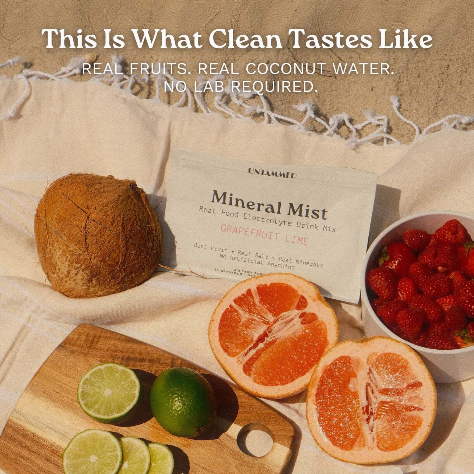 Flat lay of UNTAMMED Mineral Mist Grapefruit Lime electrolyte drink mix pouch on a beach blanket with coconut, grapefruit, limes, and strawberries. Headline: This Is What Clean Tastes Like.