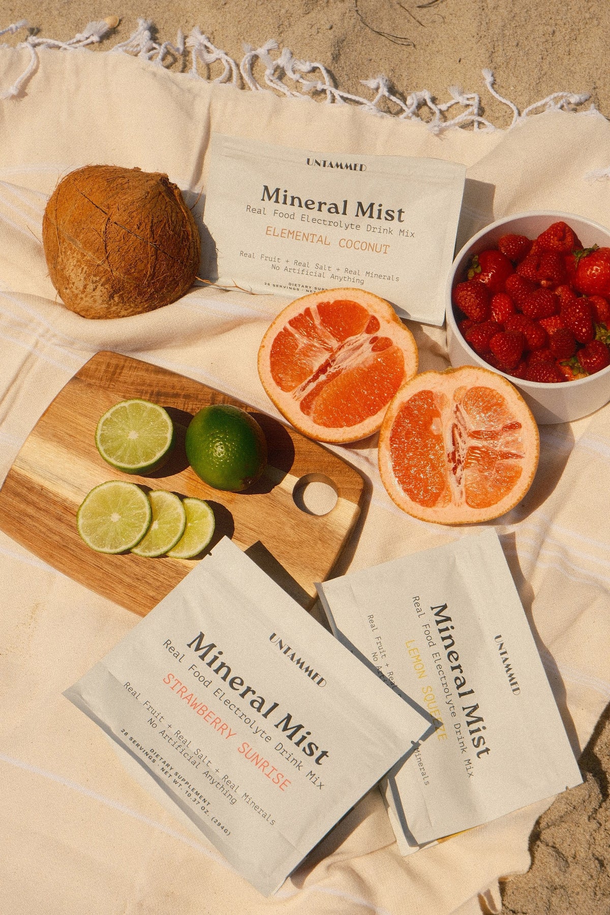 Mineral Mist pouches with coconut, grapefruit, limes and strawberries on a beach blanket