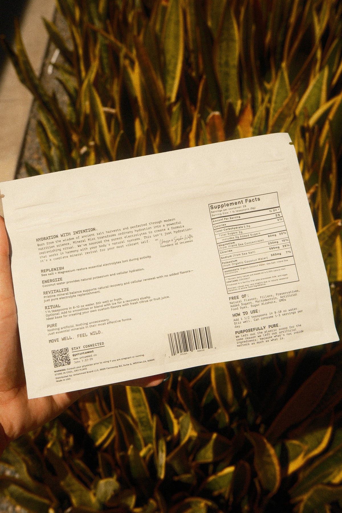 The back label of a Mineral Mist pouch held up in front of green leaves