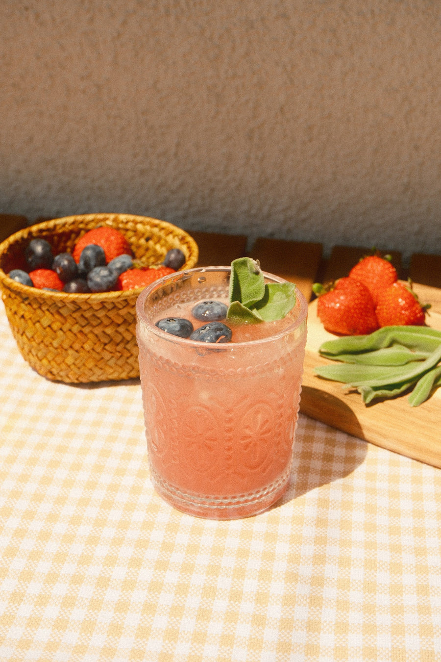 A glass of Berry Sweet Mineral Mist with blueberries and mint on a gingham cloth